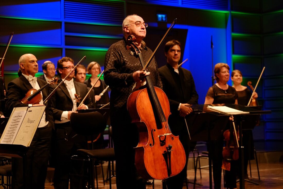 Alexander Kaganovsky on stage with his cello and bow, standing in front of the orchestra